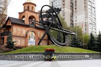 На фоні цегляної церкви та багатоповерхового будинку височіє пам’ятник жертвам Чорнобильської катастрофи у вигляді великого металевого атома на зеленому пагорбі, біля підніжжя якого на кам’яному мурі викарбувано напис «І МЕРТВИМ, І ЖИВИМ, І НЕНАРОДЖЕННИМ...» та покладено свіжі квіти.