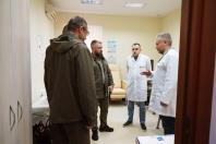 У світлому медичному кабінеті, обладнаному бежевим процедурним кріслом та інформаційними плакатами, двоє чоловіків у тактичному одязі кольору хакі ведуть серйозну розмову з двома лікарями в білих халатах, один з яких жестикулює рукою, роз'яснюючи деталі робочого процесу.