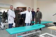 У просторій світлій залі реабілітації з великими дзеркалами та тренажерами молодий медик у білому халаті вказує рукою на сучасні масажні столи з яскраво-бірюзовою оббивкою, проводячи огляд приміщення для групи офіційних осіб у тактичному та цивільному вбранні