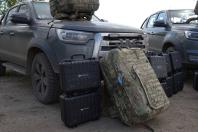 Перед темно-сірим пікапом JAC на ґрунті стоять стоси чорних захисних кейсів із маркуванням «DJI Matrice 4T» та великий камуфляжний тактичний рюкзак, а ще один такий самий рюкзак лежить на капоті автомобіля поруч із іншою автівкою на задньому плані