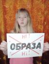 На фоні яскраво-помаранчевої текстурованої завіси світловолоса дівчинка тримає перед собою білий аркуш із великим чорним написом «ОБРАЗА», який перекреслений жирним червоним хрестом і оточений заперечними словами «Ні!».