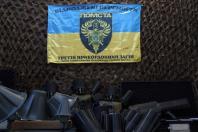 На тлі коричневої маскувальної сітки закріплений синьо-жовтий прапор бригади «Помста» 3-го прикордонного загону із зображенням орла та тризуба, а під ним на передньому плані розташоване різноманітне технічне обладнання, зокрема численні сірі конусоподібні антени та відкриті кейси зі спеціальним спорядженням