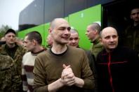На світлині під відкритим небом зображено групу щойно звільнених з полону українських чоловіків із коротко стриженим волоссям, серед яких на передньому плані виділяється емоційний чоловік у коричневому світшоті, котрий міцно стискає долоні разом із виразом глибокого полегшення та сльозами на очах, стоячи на тлі великого зеленого автобуса поруч із побратимами у військовому та цивільному одязі