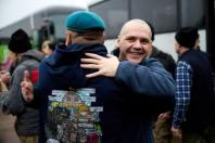 На світлині зафіксовано зворушливий момент зустрічі двох чоловіків, де на передньому плані щиро усміхнений лисий чоловік у синій кофті міцно обіймає за плечі побратима в бірюзовому береті, що стоїть спиною до кадру в худі з великим кольоровим малюнком та написом «Донеччина», а на розмитому задньому плані видно автобус та інших людей у зимовому одязі