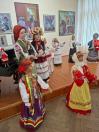 У виставковій залі поруч із картинами на стінах двоє дівчаток у традиційному українському вбранні стоять на дерев'яному подіумі серед численних великих ляльок у різнобарвних народних строях