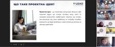Скриншот онлайн-презентації програми «U-LEAD з Європою», де ліворуч відображено слайд із заголовком «ЩО ТАКЕ ПРОЄКТНА ІДЕЯ?», визначенням цього терміна та фотографією дівчини з ноутбуком біля вікна, а праворуч — вертикальну панель із вікнами учасників відеоконференції.