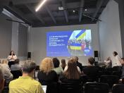 Презентація у великій залі з темною стелею, де глядачі в кріслах дивляться на проекційний екран із заголовком «СТАРОБІЛЬЩИНА: ХРОНІКИ СУПРОТИВУ ТА ДОСВІД СОЛІДАРНОСТІ» та фотографією патріотичного мітингу з українськими прапорами, поки ліворуч біля екрана виступає жінка у вишиванці