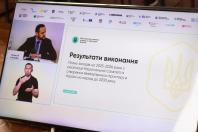 Фотографія екрана монітора, на якому відображено презентаційний слайд Міністерства розвитку громад та територій України про результати виконання Плану заходів на 2025–2026 роки з безбар'єрності, із віконцем доповідача Олексія Кулеби та віконцем сурдоперекладача ліворуч