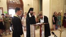 Православні священнослужителі проводять релігійний обряд біля аналоя в храмі, де один із них у чорному каптурі благословляє присутніх парафіян, які уважно спостерігають за дійством.