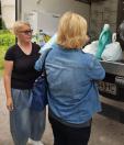 Дві жінки зі світлим волоссям розмовляють біля відчиненого кузова вантажівки, заповненого картонними коробками, пакетами та бірюзовою пляшкою з побутовою хімією.
