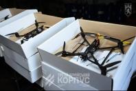 На фото зображено кілька відкритих білих картонних коробок, у кожній з яких лежить чорний FPV-дрон (квадрокоптер), розкладений на столі в темному приміщенні з логотипом «Третій армійський корпус».