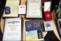 На дерев'яному столі розкладено різні нагороди та відзнаки Національної поліції України та Сухопутних військ, серед яких є офіційні подяки у рамках, медалі, нагрудний хрест у футлярі, погони полковника та коробка зі смарт-годинником Garmin.