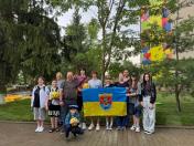 На зеленому лужку перед багатоповерхівкою стоїть група дорослих та підлітків, які тримають синьо-жовтий прапор із гербом міста Покровськ і кілька жовтих футбольних м'ячів, позуючи для спільного фото.