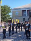 Ряд дівчат-поліцейських у темній формі урочисто несуть кошики із синьо-жовтими квітами брукованою площею на тлі пам'ятника Тарасові Шевченку, великої будівлі з балконом та людей із державними прапорами України.