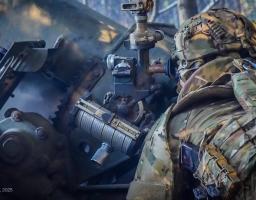 Український артилерист готується до чергового пострілу, уважно звіряючи приціл на позиції ворога в лісосмузі. Серед ретельно замаскованих гармат і техніки він зосереджено працює з оптичним приладом, перетворюючи координати розвідки на точний вогонь. Захисник у сучасному камуфляжі й шоломі символізує витривалість і професіоналізм української армії, що тримає оборону на передовій
