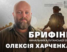 Крупний план бородатого чоловіка на ім'я Олексій Харченко, який носить сорочку кольору хакі, розташований поруч із текстом «БРИФІНГ НАЧАЛЬНИКА ЛУГАНСЬКОЇ ОВА» та емблемою адміністрації, а праворуч на тлі заходу сонця видно силует солдата.