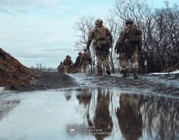 Кілька українських військовослужбовців із 46-ї окремої аеромобільної бригади йдуть по розмитій ґрунтовій дорозі з калюжами та снігом на узбіччі