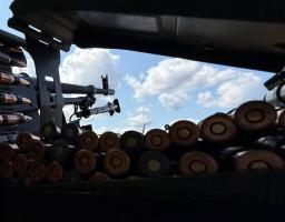 Вид ізсередини бойової позиції або військової техніки, що демонструє великокаліберний кулемет та численні боєприпаси, спрямовані на тло блакитного неба з хмарами