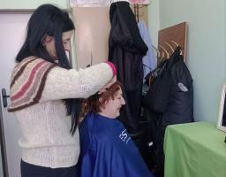Жінка-перукар із темним волоссям стоїть і стриже коротке руде волосся клієнтки, яка сидить у синій накидці в салоні краси