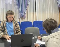 Дві людини сидять за столом в офісному приміщенні, одна працює за ноутбуком HP, а інша пише на папері
