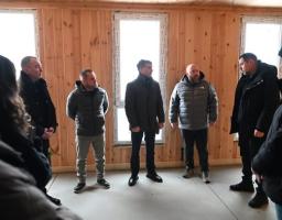 Кілька чоловіків у зимовому одязі стоять у кімнаті з дерев’яними стінами, обговорюючи будівництво житлового комплексу для внутрішньо переміщених осіб на Закарпатті. Вони, зокрема, включають голову Луганської обласної військової адміністрації та голову Закарпатської обласної державної адміністрації Мирослава Білецького.