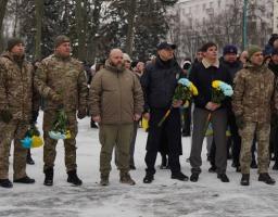 Група чоловіків у військовій формі стоять на вулиці взимку, деякі тримають букети синьо-жовтих квітів.