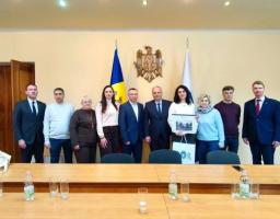 На зображенні група з десяти людей, одягнених в офіційний та напівофіційний одяг, позує для фотографії в приміщенні для засідань. На задньому плані видно прапор та герб Республіки Молдова. Люди стоять за дерев'яним столом, а двоє в центрі тримають аркуш паперу або сертифікат