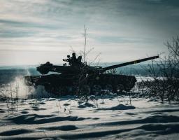 На зображенні показано силует танка Т-72 на засніженому полі, з яскравим небом на задньому плані та сухими кущами на передньому