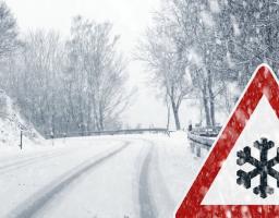 Зображення демонструє засніжену гірську дорогу взимку, на узбіччі якої розташований попереджувальний дорожній знак про ожеледицю або снігопад