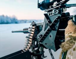 На фотографії зображено крупнокаліберний кулемет, встановлений на турелі та оснащений оптичним прицілом, який використовує військовослужбовець у польових умовах