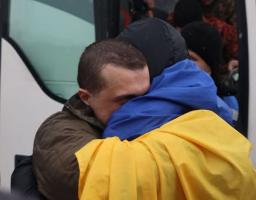 Український військовослужбовець та близька людина тепло обіймаються, причому одна особа загорнута в синьо-жовтий прапор
