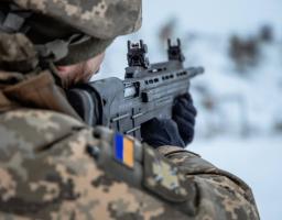 На світлині зображений український військовослужбовець у піксельному камуфляжі, який цілиться з автоматичної гвинтівки «Малюк» (Вулкан-М) на тлі засніженого краєвиду. На плечі бійця чітко видно шеврон із національним прапором та тактичним знаком, що підкреслює його приналежність до Сил оборони України