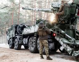 На цьому зображенні українські військовослужбовці працюють із вітчизняною самохідною артилерійською установкою (САУ) 2С22 «Богдана» у зимовому лісі. Один боєць розрахунку перебуває на сидінні навідника біля гармати, а інший стоїть поруч із великогабаритною колісною платформою, ймовірно, на шасі Tatra