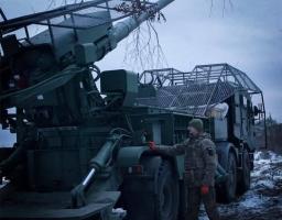 Українська 155-мм самохідна артилерійська установка 2С22 «Богдана» на бойовій позиції. Артилерист 54-ї окремої механізованої бригади стоїть поруч із установкою на засніженій місцевості.