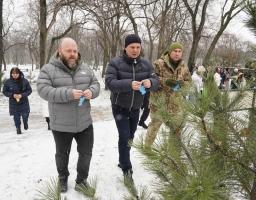 Учасники меморіальної акції в засніженому парку вішають паперових янголів на гілки сосни в пам'ять про загиблих дітей.