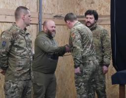 Нагородження бійців 3-ї окремої штурмової бригади. Військовий у тактичному одязі тисне руку штурмовику на фоні прапора Хорунжої служби бригади