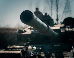 На фото зображено крупний план ствола гармати українського танка 31-ї окремої механізованої бригади, спрямованого вперед на тлі розмитого пейзажу та екіпажу