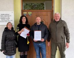 Четверо людей — три жінки та чоловік у військовій формі — стоять біля входу до Добротвірської селищної ради, тримаючи в руках офіційні документи, що свідчать про підписання меморандуму або угоди про співпрацю