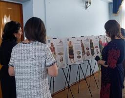 Троє жінок розглядають виставку інформаційних постерів на мольбертах, що демонструють різноманітні зразки традиційного українського вбрання з ілюстраціями та описом їхніх особливостей.