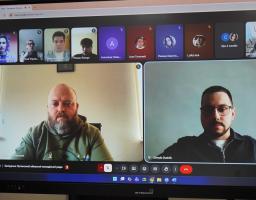 На моніторі марки «INTBOARD» відображено вікно онлайн-зустрічі в Google Meet, де учасники засідання Луганської обласної молодіжної ради, серед яких двоє чоловіків на передньому плані та декілька інших у мініатюрах зверху, обговорюють робочі питання в режимі відеоконференції.