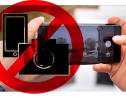 Руки людини тримають смартфон у горизонтальному положенні, роблячи знімок міської архітектури або парку. На екрані телефона видно інтерфейс камери.