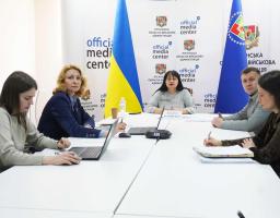 П’ятеро учасників засідання в «Official Media Center» Луганської обласної військової адміністрації сидять за білим Т-подібним столом із ноутбуками та паперами на фоні прапорів України та брендованих банерів.