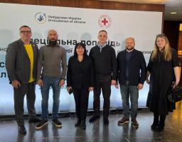 Група з шести офіційно вдягнених людей — чотирьох чоловіків і двох жінок — позують для спільного фото на фоні банера з логотипами Омбудсмена України та Червоного Хреста під час презентації спеціальної доповіді.