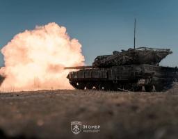 На фото зображено український танк (імовірно Leopard 1A5 або модернізований Т-64), оснащений додатковим захистом. Зокрема, помітно маскувальну сітку на башті та навісні елементи динамічного захисту на корпусі й бортах.