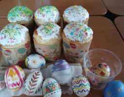 На дерев'яному столі розміщена святкова великодня композиція, що складається з шести апетитних пасок у декоративних паперових формах, покритих білою глазур'ю з різнокольоровою посипкою, та ряду власноруч розписаних писанок із різноманітними візерунками й орнаментами.