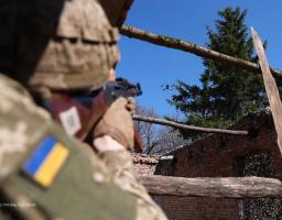 зображено українського військовослужбовця у напівпрофіль зі спини. Він перебуває всередині напівзруйнованої цегляної будівлі без даху. Солдат цілиться з автомата Калашникова у невеликий квадрокоптер, що завис у синьому безхмарному небі.