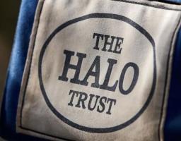 Макрофотографія нашивки міжнародної організації «The HALO Trust» на темно-синій тканині, де на світлому фоні всередині овальної рамки розміщено назву фонду великими друкованими літерами