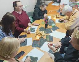 У невеликому кабінеті з мапою Європи та календарем на стіні п’ятеро жінок різного віку сидять навколо довгого дерев’яного столу, зосереджено працюючи над творчими малюнками в техніці подряпування на чорному фоні, а поруч із ними стоять стакан з олівцями, тарілка з печивом та запалена свічка