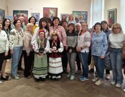 Велика група людей, переважно жінок у сучасному та традиційному українському одязі, стоїть разом у музейній залі на тлі розвішаних на стінах картин, а в центрі першого ряду знаходяться двоє дівчаток у вишиванках та вінках з обрядовими ляльками-мотанками в руках