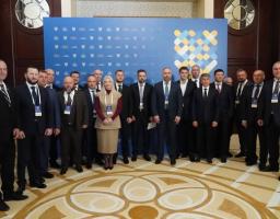 Група людей у ділових костюмах, серед яких одна жінка, стоїть на тлі синьо-жовтого банера під час офіційного заходу